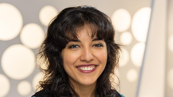 A headshot of a woman with a dark brown shag haircut smiling against a white background.